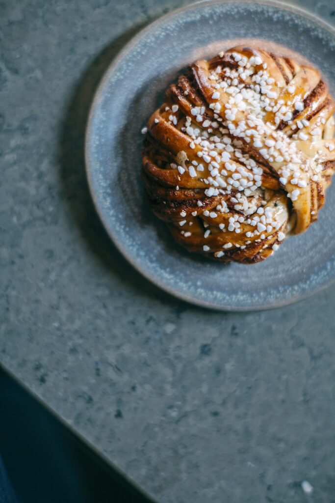 En kanelbulle med pärlsocker som ligger på ett fat placerat på bänk